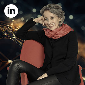 Corinne Nauber sitzt schräg auf einem Stuhl, oben links das LinkedIn-Logo